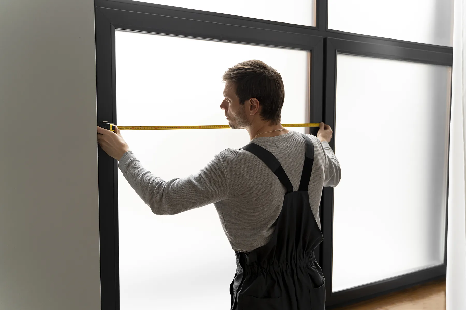 Technician measuring a window opening with tape measure — Renossance explains factors influencing the cost of window installation.