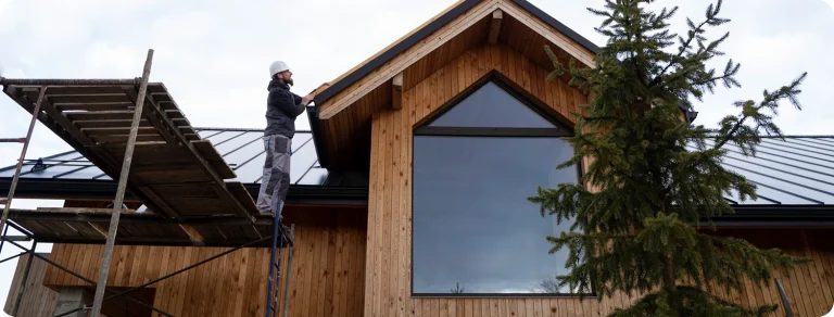 Worker on scaffolding installing siding on wooden house exterior — professional siding installation and repair service
