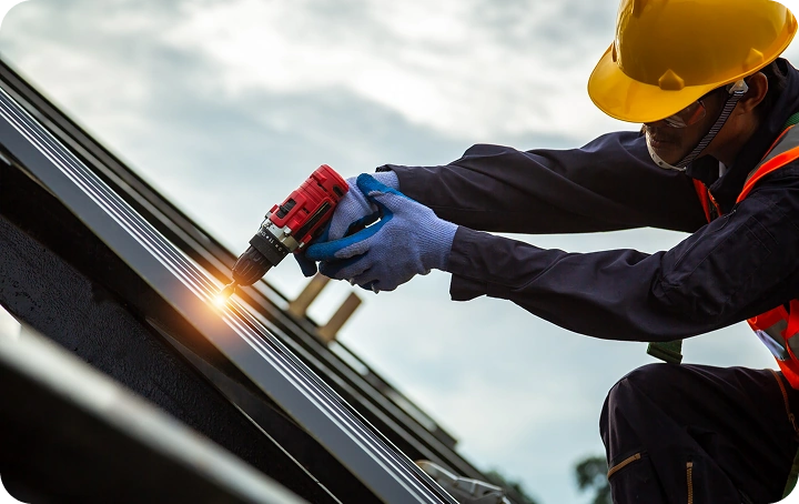 Roofer in hard hat and safety vest using power tool on metal roof — professional roof repair service