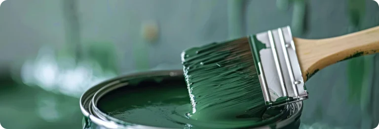 Paintbrush dipped in green paint can — professional painting services for interior and exterior