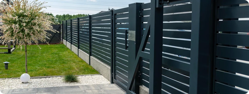 Modern horizontal slat fence installation in dark charcoal grey aluminum with matching sliding gate, green lawn and garden in background