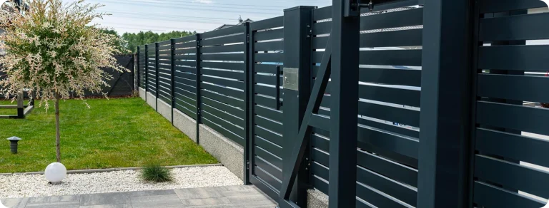 Modern horizontal slat fence installation in dark charcoal grey aluminum with matching sliding gate, green lawn and garden in background