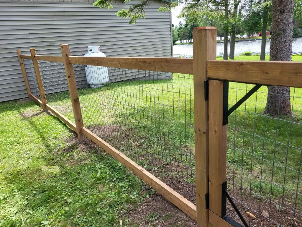 Wooden fence with metal wire mesh on a green lawn near a house. Fence installation and fence repair in Stirling.